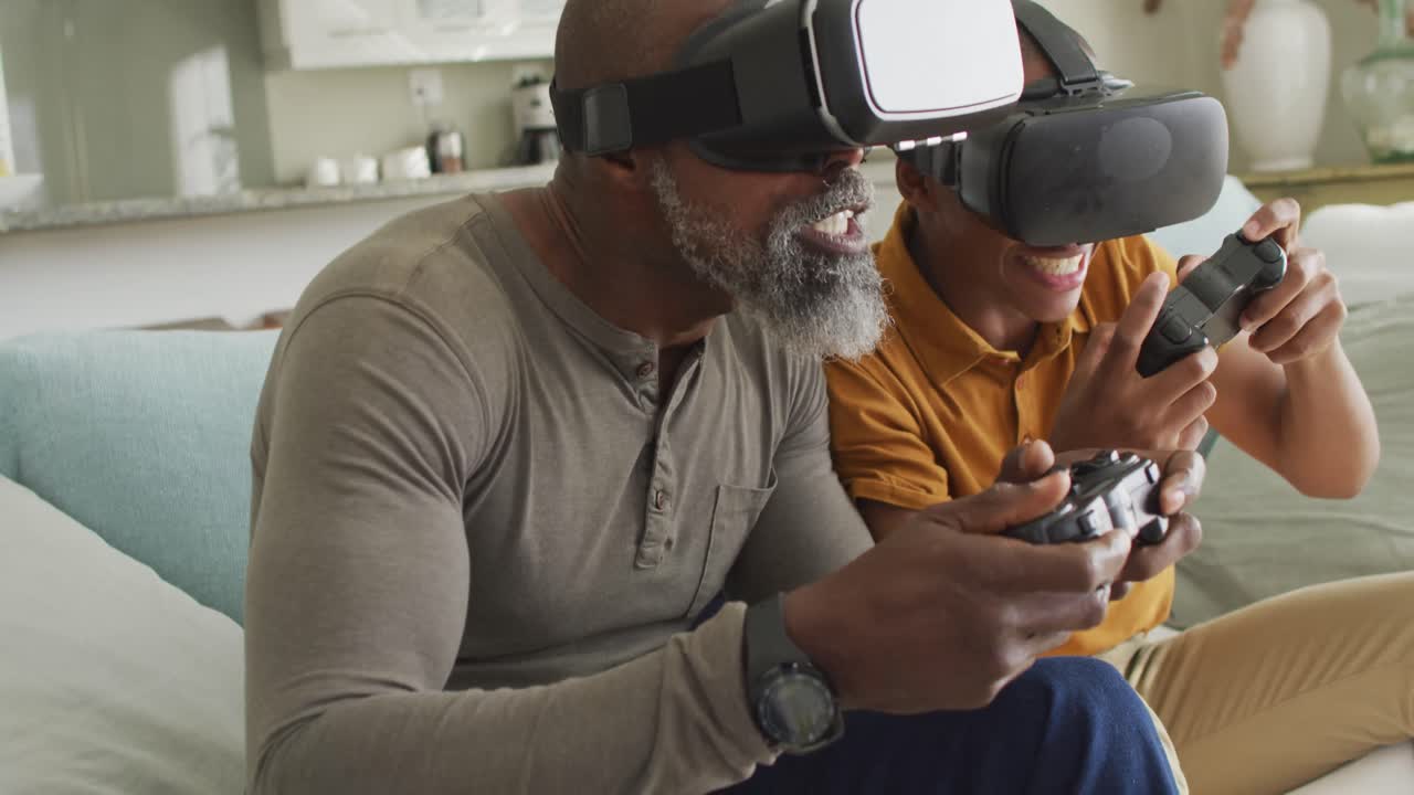 Video of happy african american father and son wearing vr headsets and playing video games