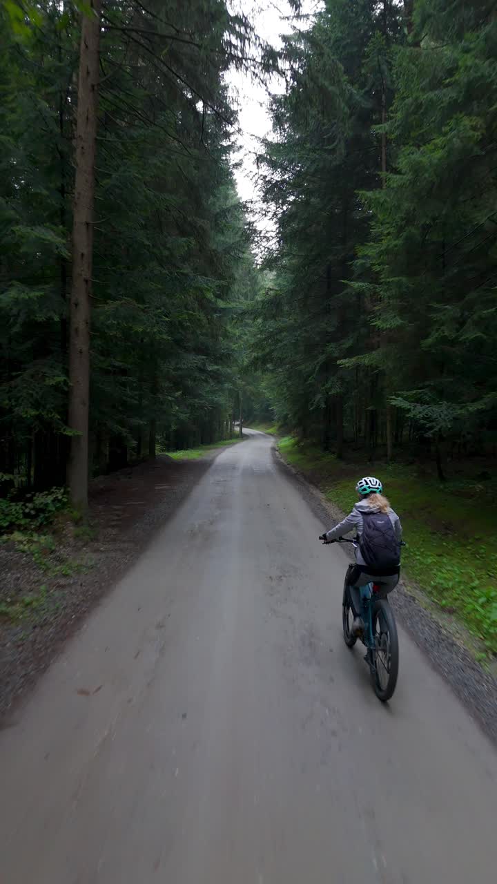 Femme faisant du vélo électrique sur un chemin forestier entouré d’une nature verdoyante, vue verticale de suivi