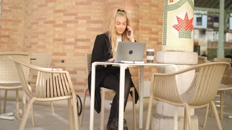 woman talking on smartphone while working with laptop in cafe