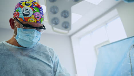 male bearded surgeon in funny cap, glasses and mask focused on performed procedure. portrait of a doctor engaged in surgery. low angle view.