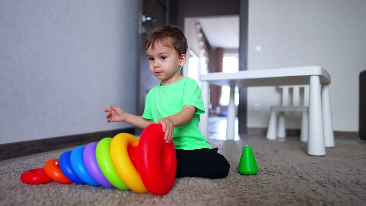Beautiful kid pushing toy pyramid on the floor and disassembling it. Caucasian boy playing at home.