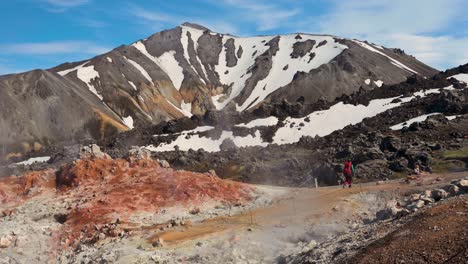 A-woman-hiker-walking-solo-through-sulfur-fumes-by-reddish-rocks-in-the-rainbow-mountains-of-Landmannalaugar-in-Iceland