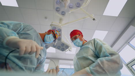 cooperating surgeons in funny bright caps work at operation. doctors use tools, equipment and discuss during work. low angle view from patient's point.