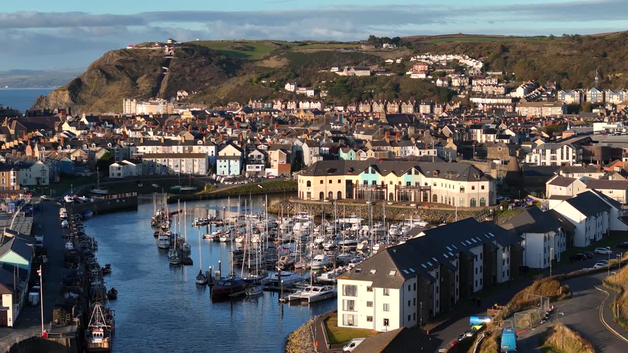 Stunning drone footage of Aberystwyth Harbour on a sunny evening, showcasing the boats, coastline, and golden hour light in a peaceful and scenic setting.
