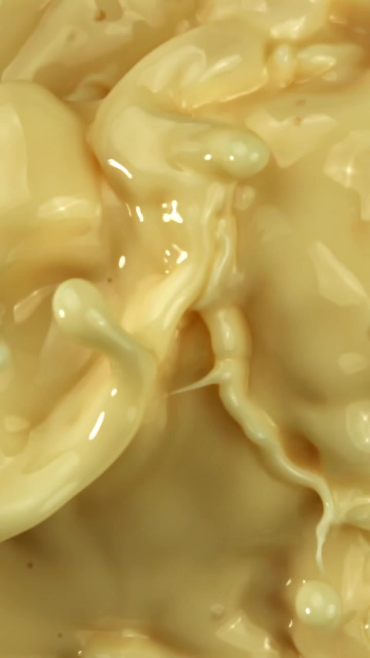 Primer plano en cámara lenta de líquido cremoso beige salpicando y arremolinándose