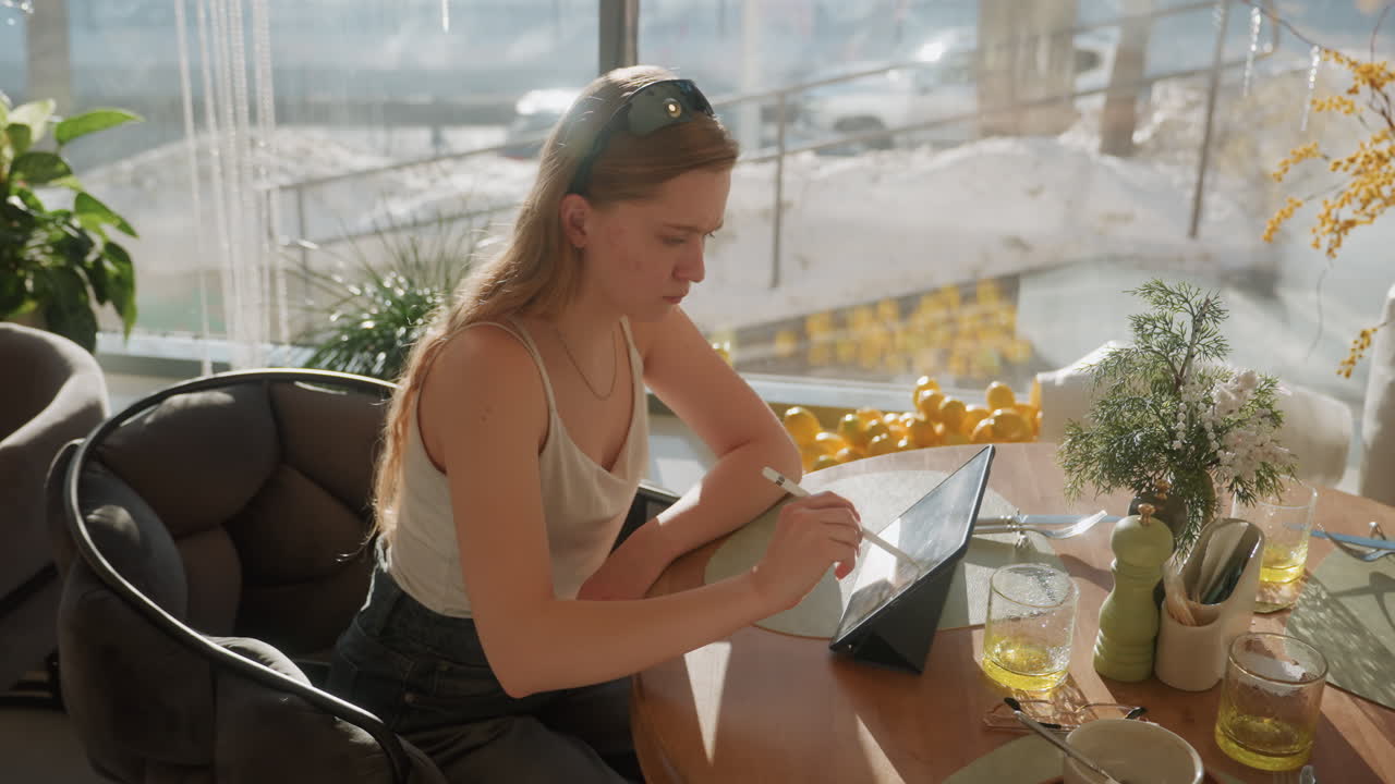Sunny corner cafe with white artist drawing on tablet, flowers and vase by window, warm backlight creating soft highlights, focused creative process and digital artwork development