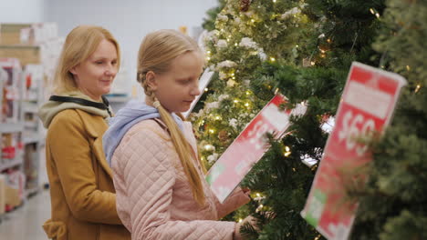 A-woman-with-a-child-chooses-a-Christmas-tree-in-the-store.-Shopping-before-the-winter-holidays