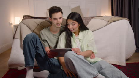 couple watching unexpected movie scene on tablet while sitting on the floor at home 1