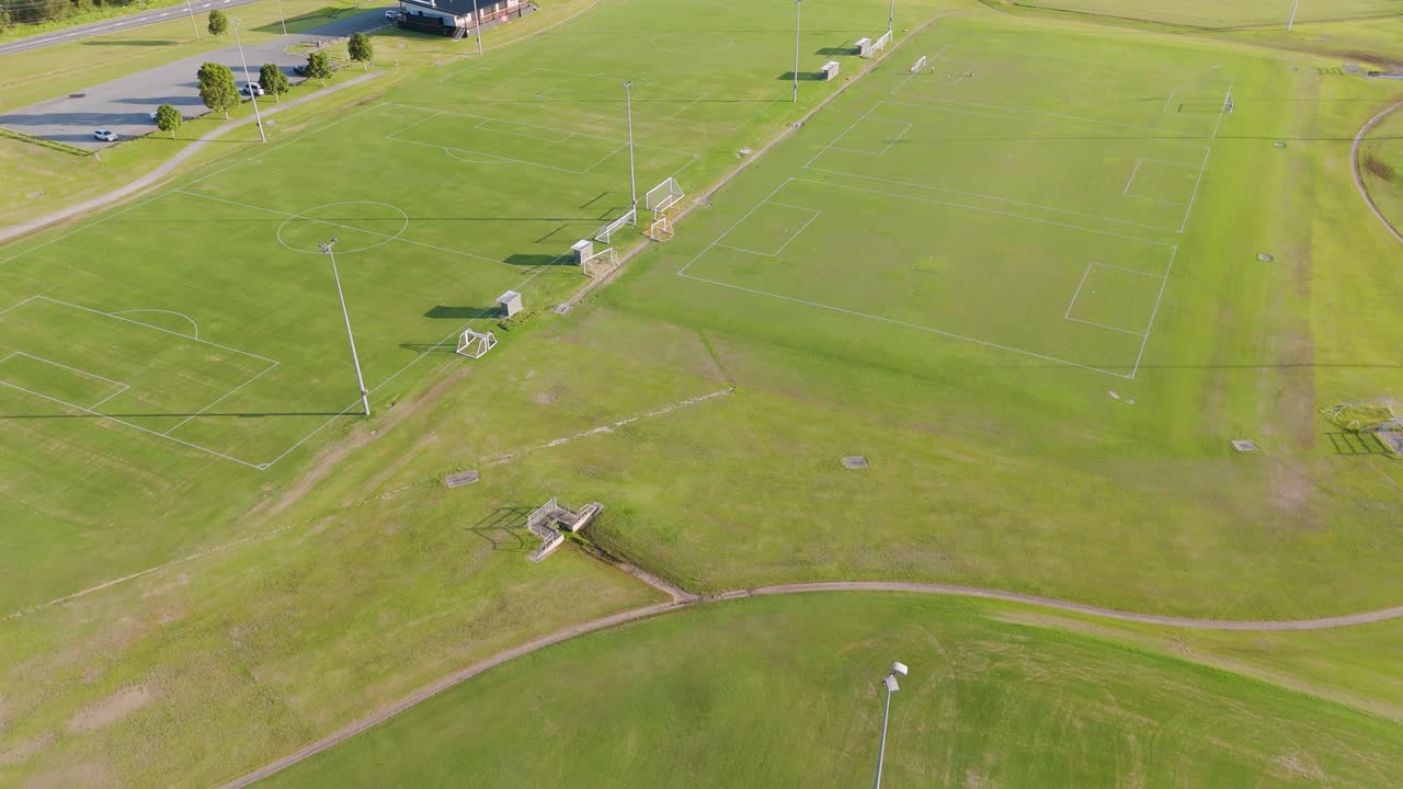Drone footage captures expansive soccer fields under bright sunlight, showcasing the layout and surrounding greenery