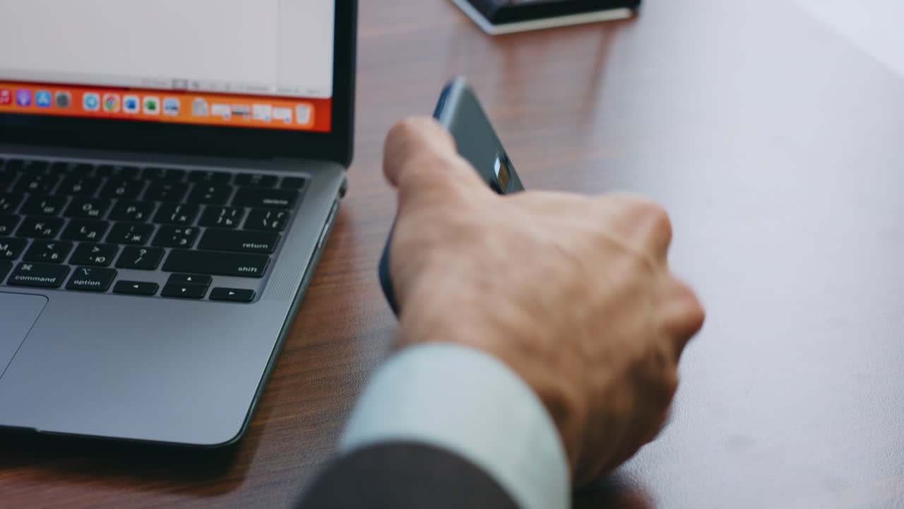 las manos del gerente de la oficina escribiendo en la computadora portátil tomando el teléfono inteligente de pantalla verde de cerca.