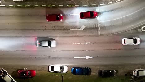 car headlights shine as they cross over faded white arrow in asphalt, drone at night