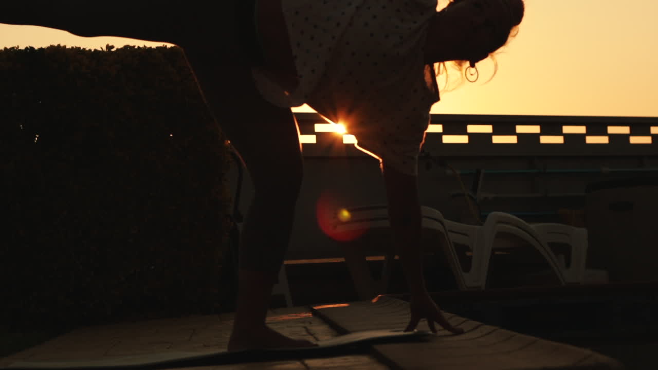 Reflection in the water of young woman do yoga pose at sunrise with a strong sun backlight