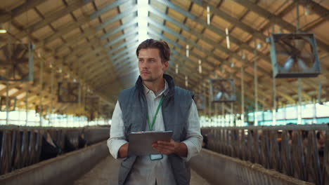 Livestock-owner-checking-animal-feedlots-making-notes-on-clipboard-at-cowshed.