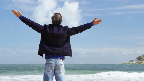 mature man standing with arms outstretched on the beach