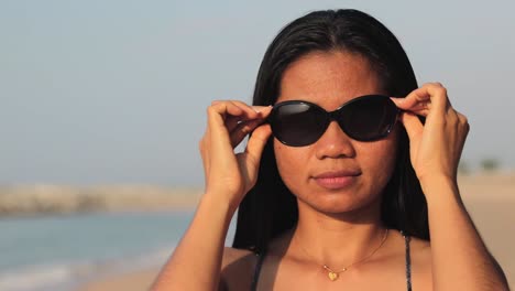 Mujer-De-Pie-En-La-Playa-Usa-Gafas-De-Sol-Para-Protegerse-En-Un-Día-Soleado-En-Verano