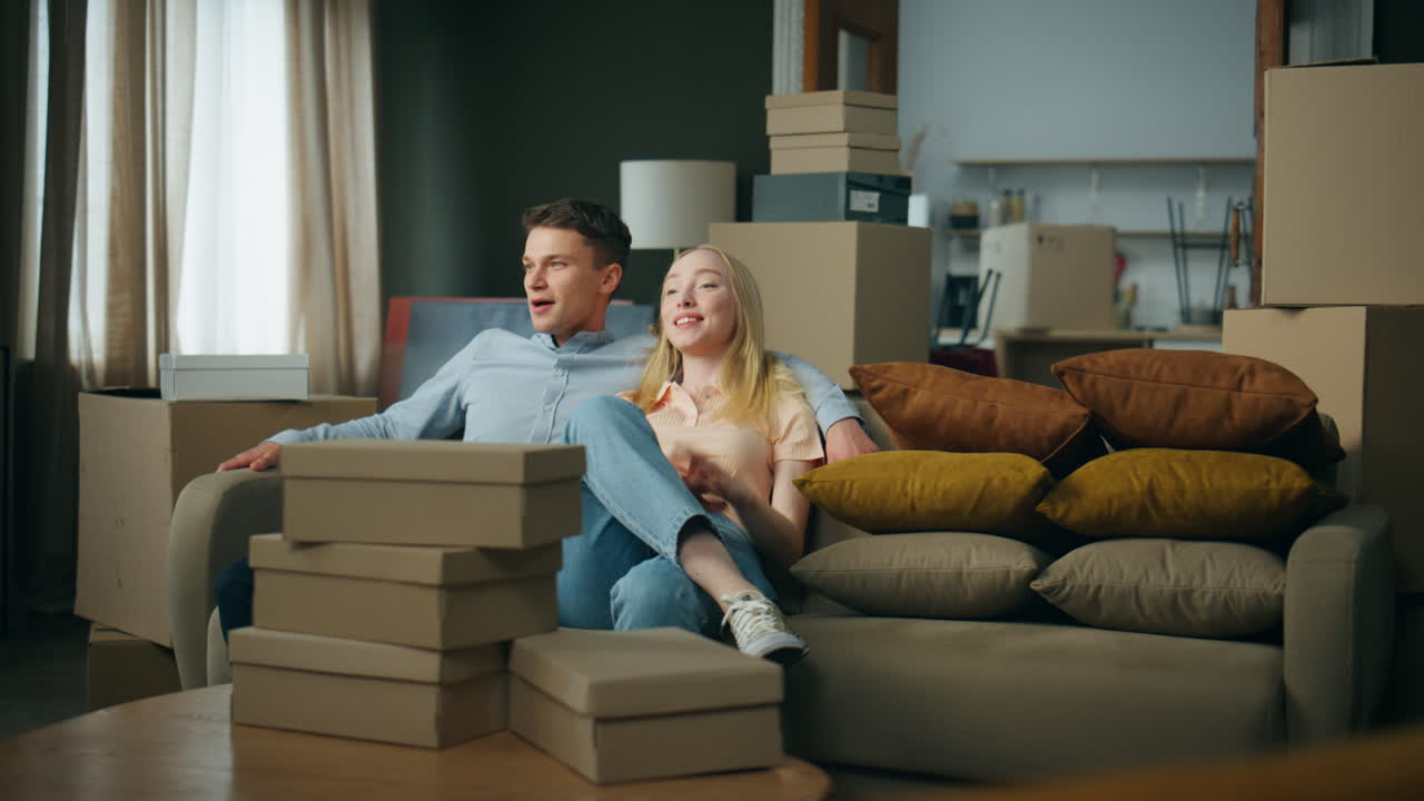 Couple sitting new sofa excited about moving house. Man hugging blond woman.