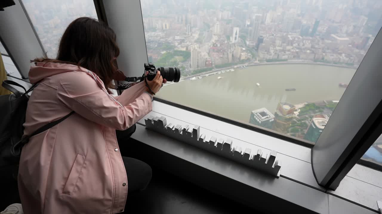 Female tourist using a full-frame camera to photograph the city from the Shanghai Tower, China