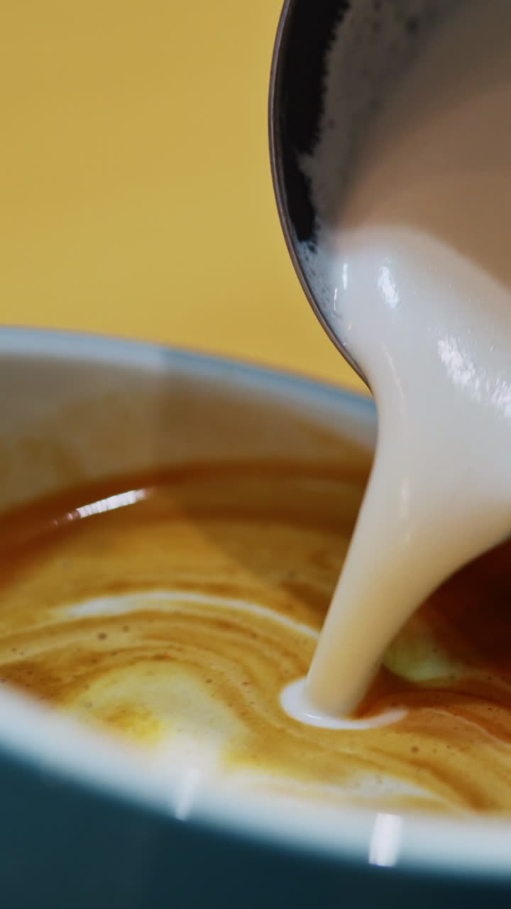 Barista making of cafe latte art. Heart shape on coffee in a cup. Making latte by pouring milk slowly into a blue cup. Close-up. Vertical video