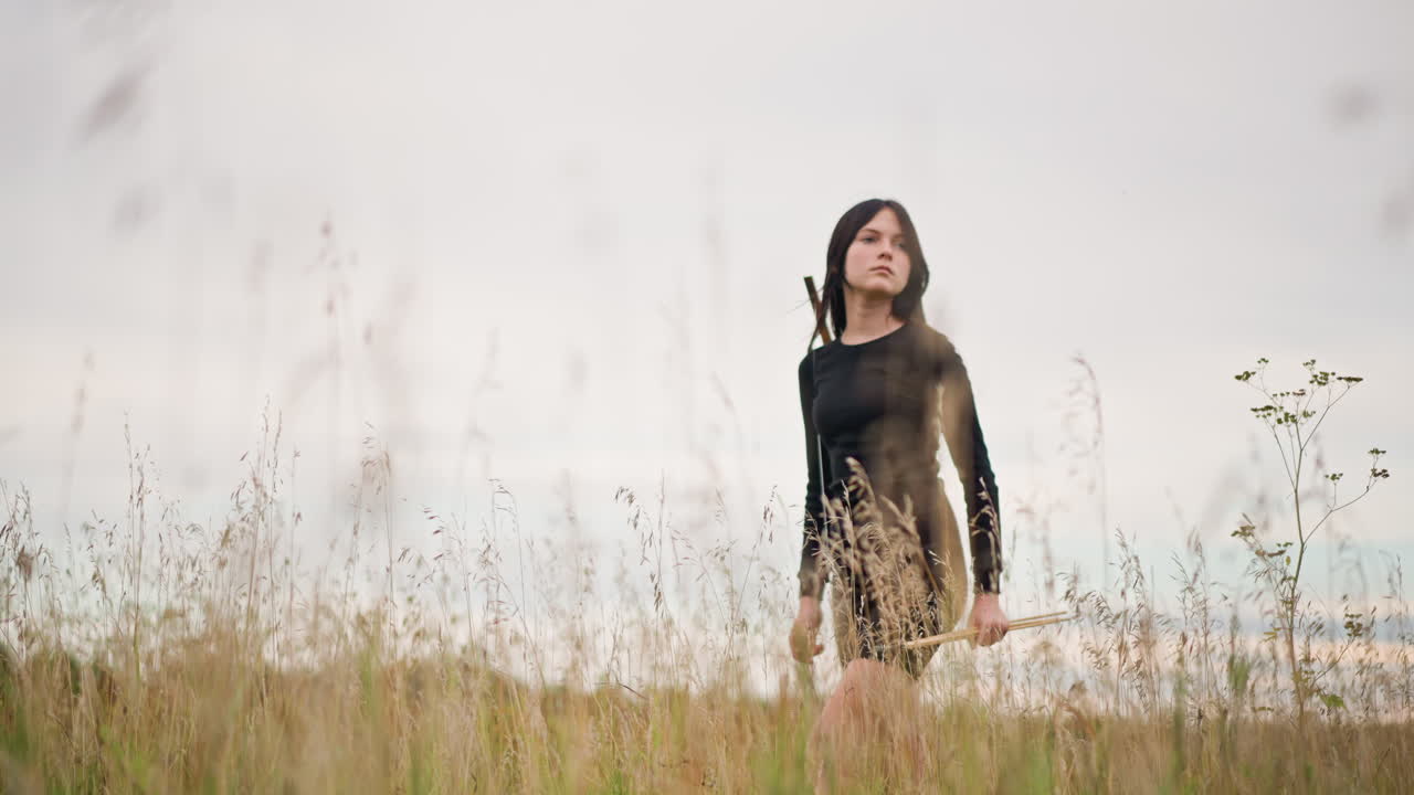 giovane donna caucasica in un prato spazzato dal vento, ritratto contemplativo di un'estetica da guerriero solitario, vestito nero, a piedi nudi, erba alta, cielo nuvoloso, nebbia leggera, orizzonte costiero, atmosfera cinematografica, introspettivo