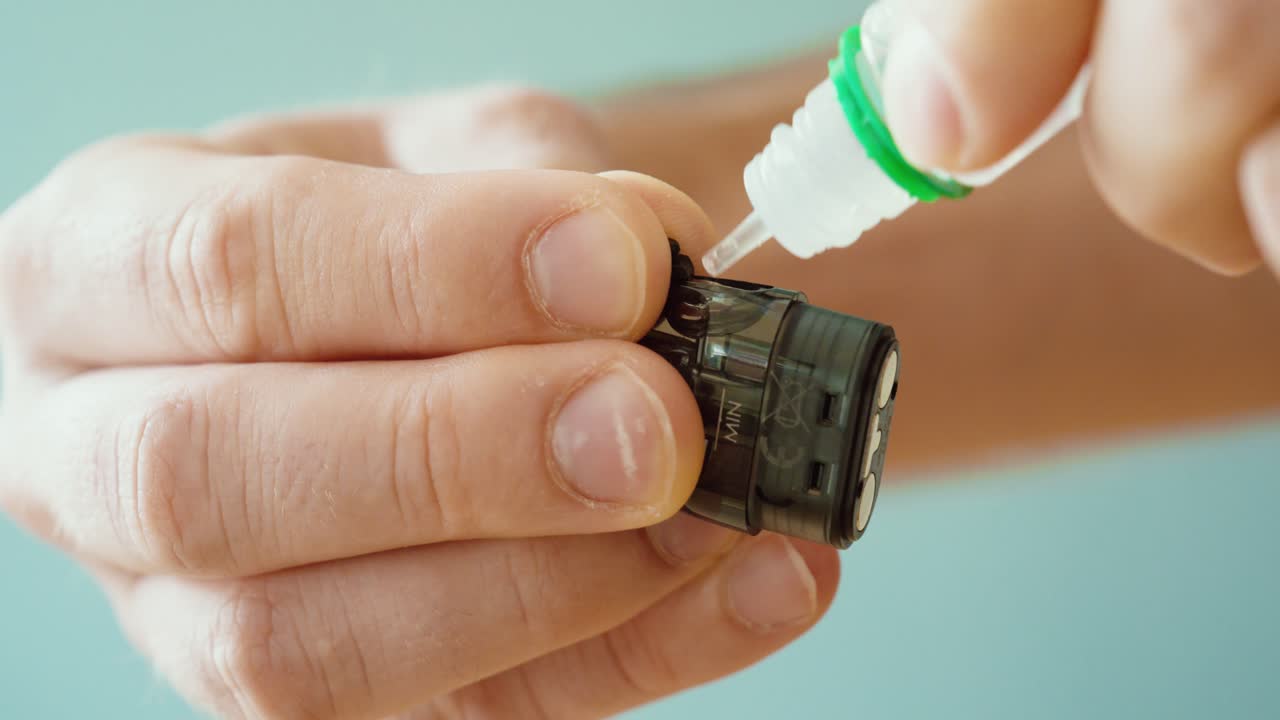 close-up of hands refilling e-liquid into a vape cartridge. Concept of e-cigarette maintenance, vaping accessories, nicotine liquid refill, and modern smoking alternatives