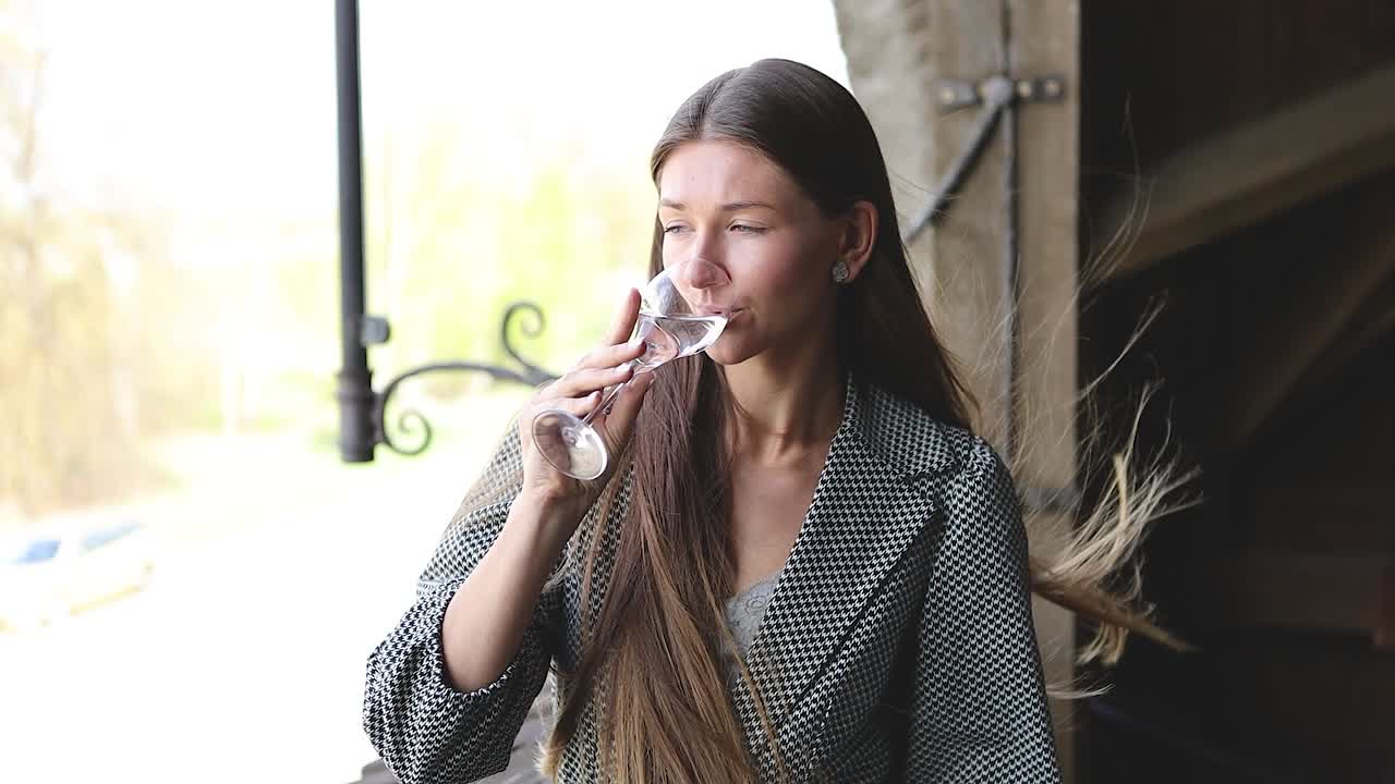 impresionante mujer joven disfrutando de una copa de champán en el balcón en un día soleado y ventoso