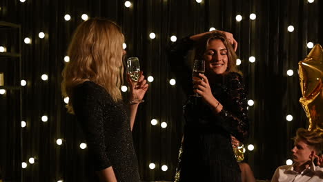 dos jóvenes mujeres bonitas bailando con una copa de champán en la mano en una fiesta de fin de año