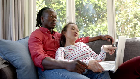 happy diverse couple relaxing on couch using laptop in sunny living room, slow motion