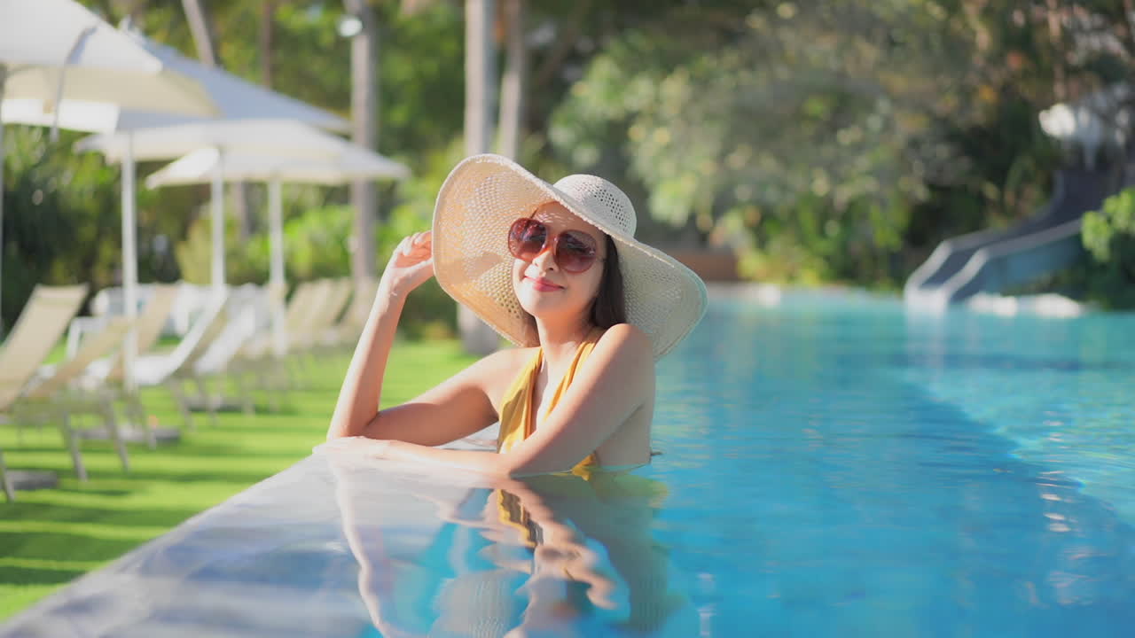 An attractive young Asian woman is chest-high in the water of her resort swimming pool
