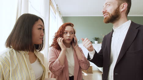 man holding his closed laptop computer and explaining something to an woman while a redhead girl using mobile phone