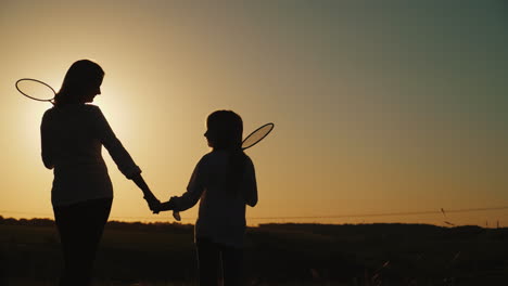 Mom-And-Daughter-Are-Standing-At-Sunset-Holding-Tennis-Rackets-Sports-Family-Leisure-Concept-4K-Vide