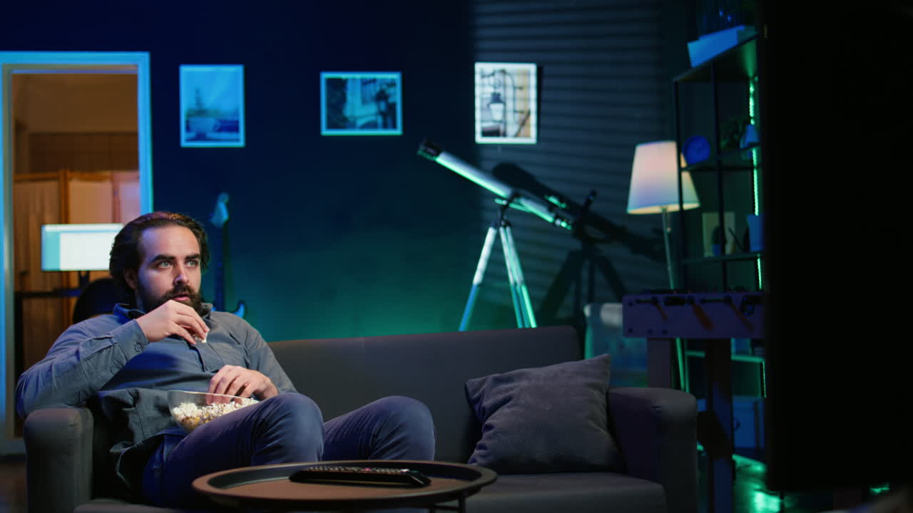 집에서 yv에서 긴장감 넘치는 영화를 보고 팝콘을 먹는 남자