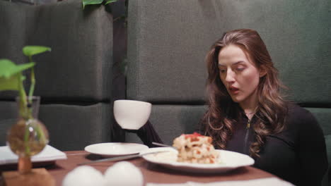 lady in black top gently sips latte while seated in cozy booth and slowly returns cup to white saucer, with creamy waffles, green plant in vase, and soft indoor lighting creating warm ambiance
