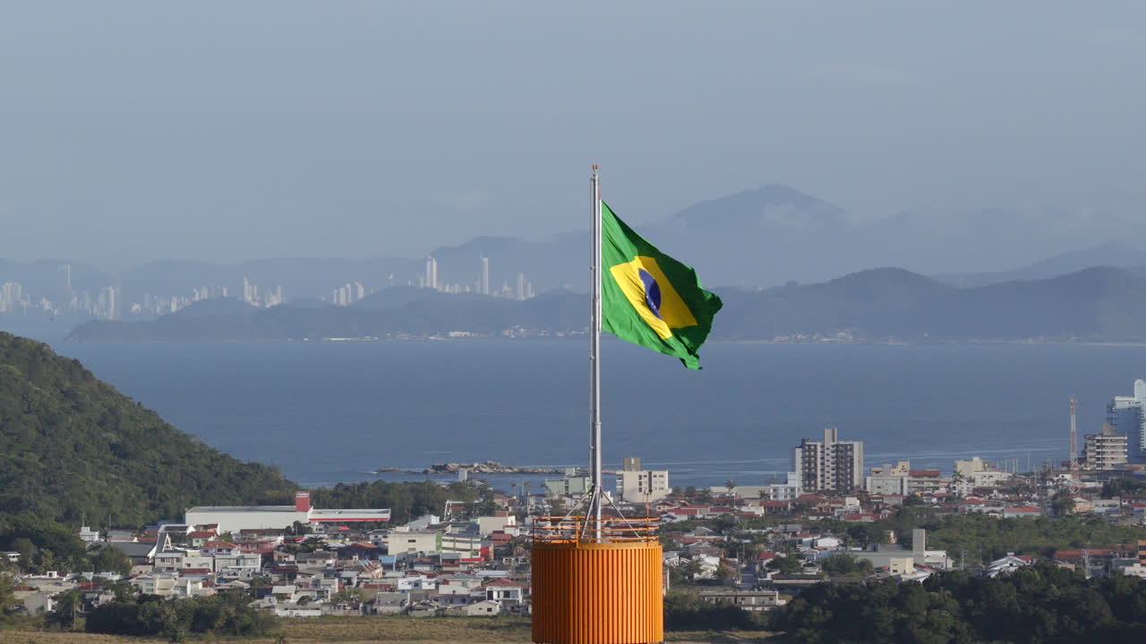Bandiera brasiliana che sventola con lo skyline delle città di Itajaí e Balneário Camboriú sullo sfondo in lontananza.