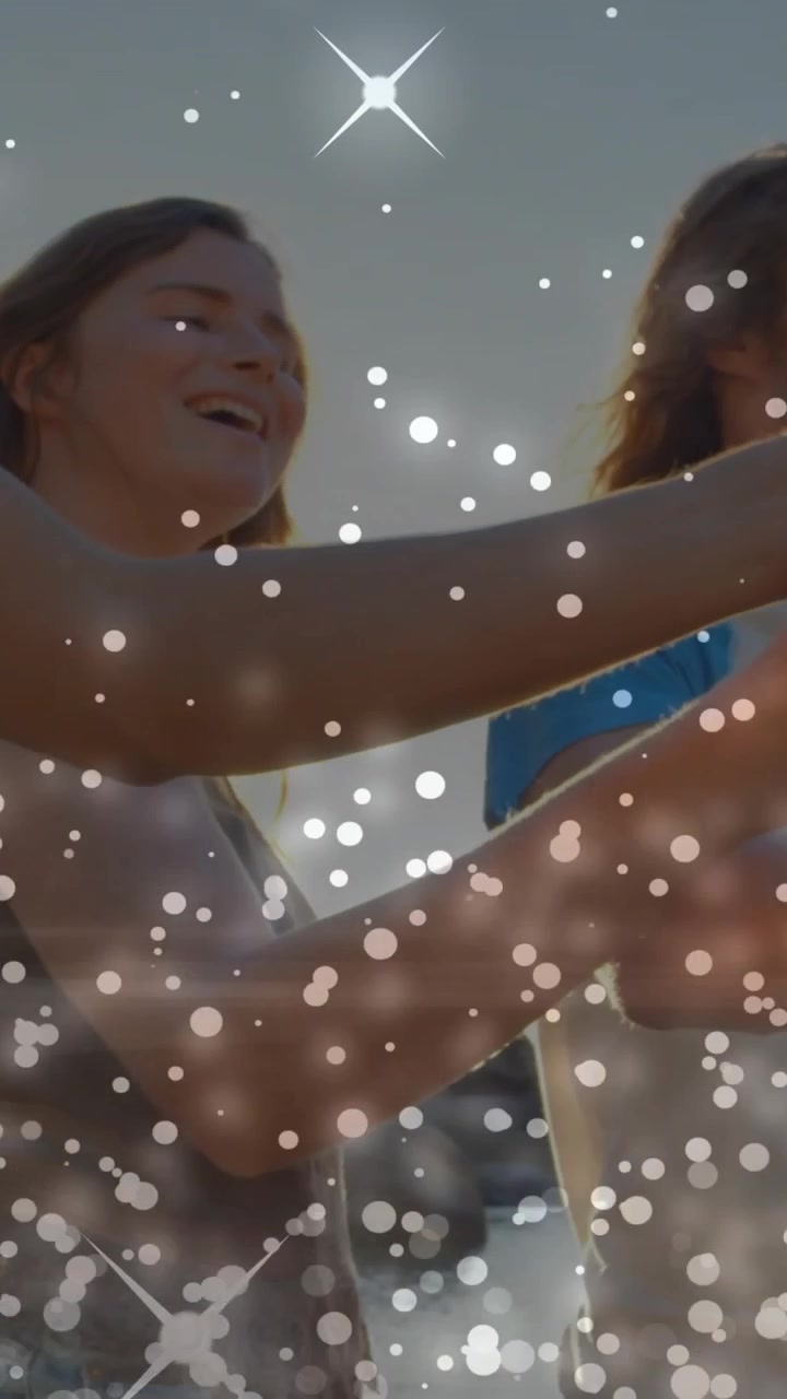 Video verticale: Donna che alza una tazza, un gruppo di amici che brinda con bicchieri rossi sulla riva, con scintille che illuminano le mani.
