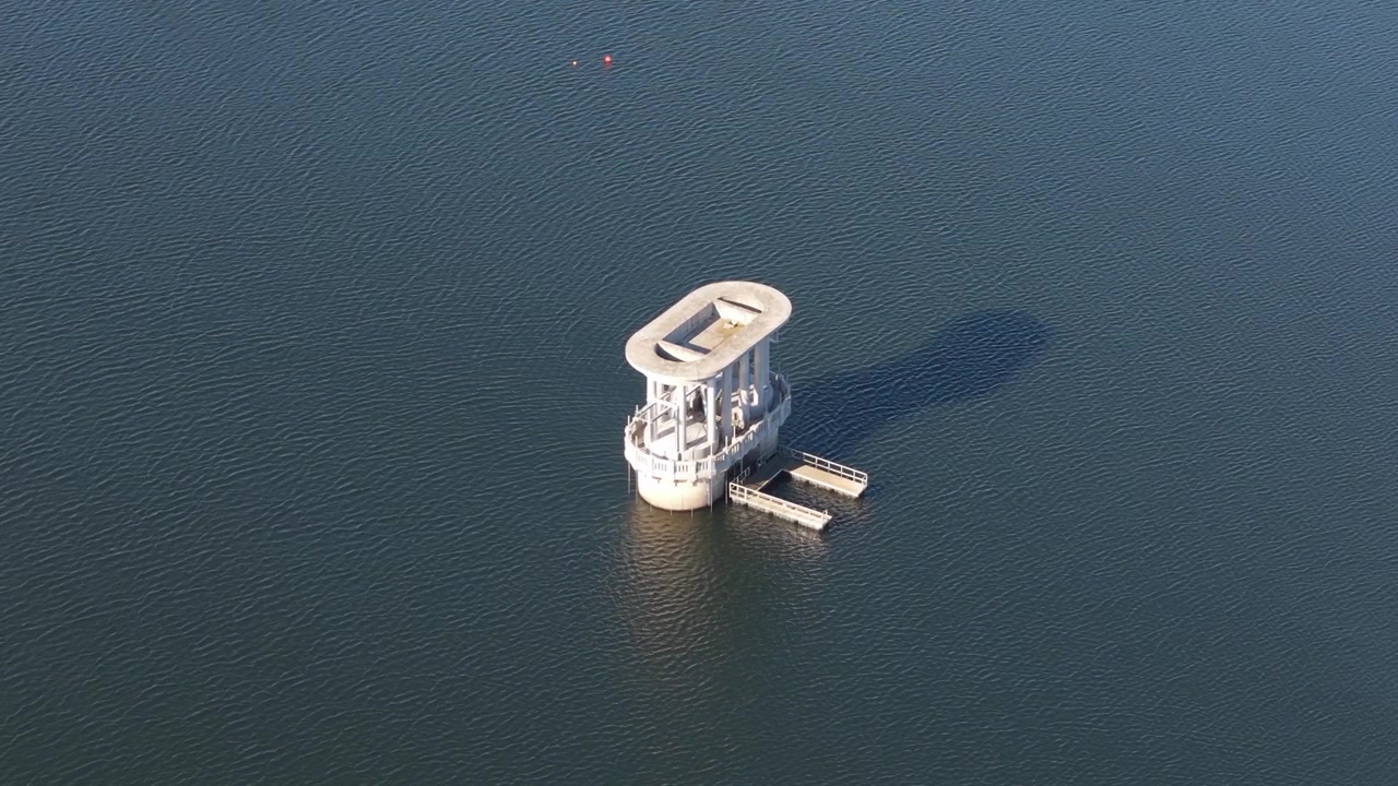 Fugleperspektiv af en betonvandindtagsstruktur, der står alene i et stort, krusende reservoir.