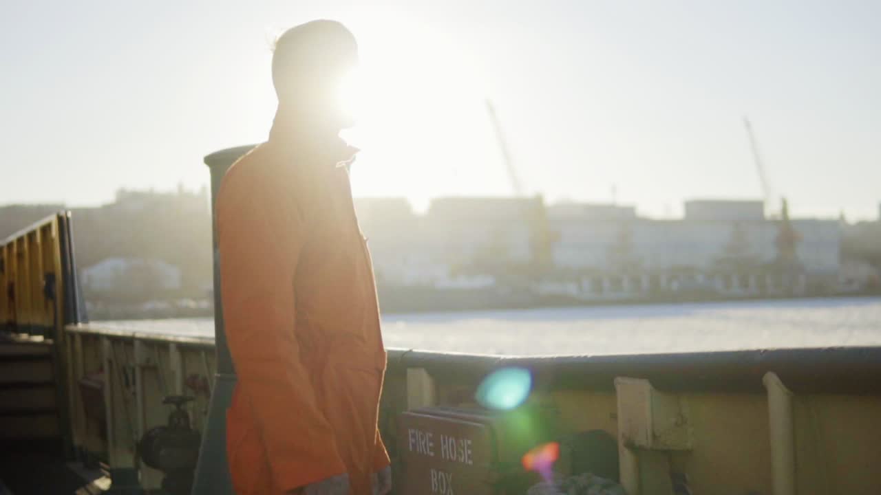 선박의 보드  ⁇ 에 서 있는 오렌지색 유니폼을 입은 항구 노동자. 렌즈 플레어. 느린 동작
