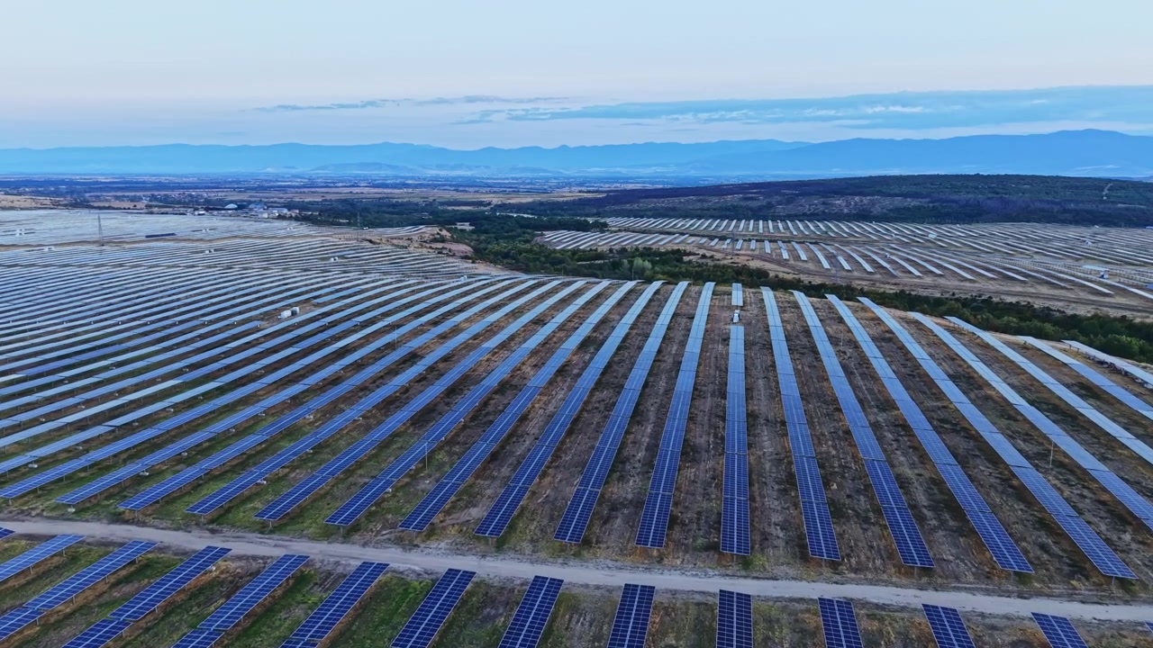 夕暮れ時の光の中、田園地帯に並ぶソーラーパネルの太陽光発電所