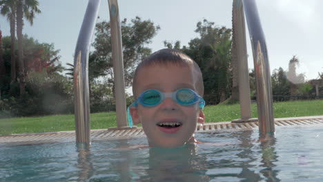 niño alegre con gafas de protección bañándose en la piscina al aire libre