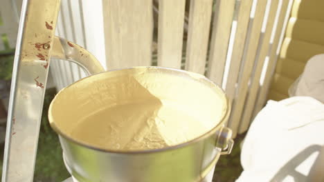 broad paintbrush dipped into bucket of yellow paint, painting of exterior wall