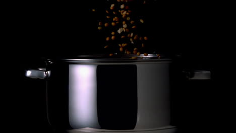 popcorn kernels falling into pot on black background