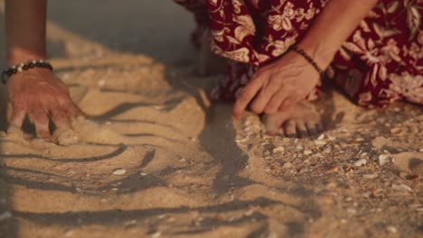 mujer joven con un vestido rojo de verano, moviendo arena con las manos en busca de conchas marinas, en una playa tropical