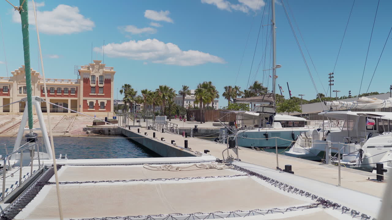 View from the window of a catamaran to a dock in the port of Valencia, Spain with views of the city's old shipyard and other sailboats