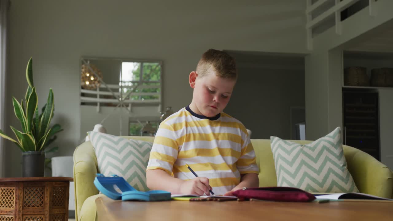 테이블에 앉아서 집에서 혼자 공부하는 백인 소년