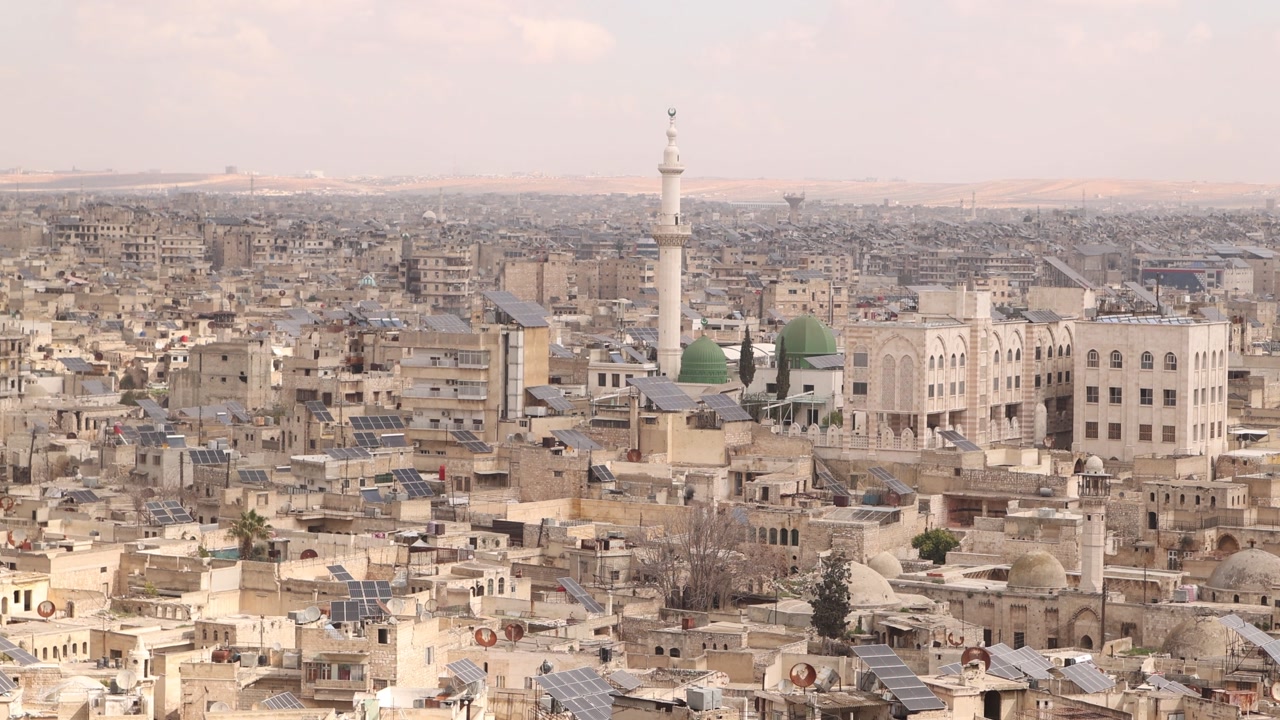Panoramic cityscape of Aleppo, Syria, featuring a white minaret and dense urban rooftops. A look at the sprawling historic and modern districts of one of the world's oldest cities