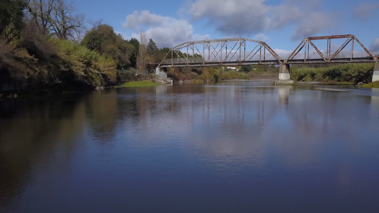 drone volando debajo de un nuevo puente de armadura con un puente viejo en el fondo del río ruso en healdsburg, california