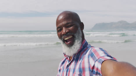 Mixed-race-senior-man-taking-a-selfie-with-a-smartphone-at-the-beach