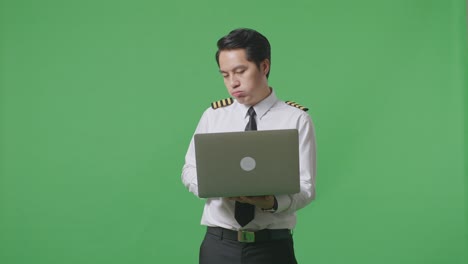 녹색 스크린 배경 스튜디오에 서 있는 동안 노트북을 사용하는 아시아 남자 조종사와 두통