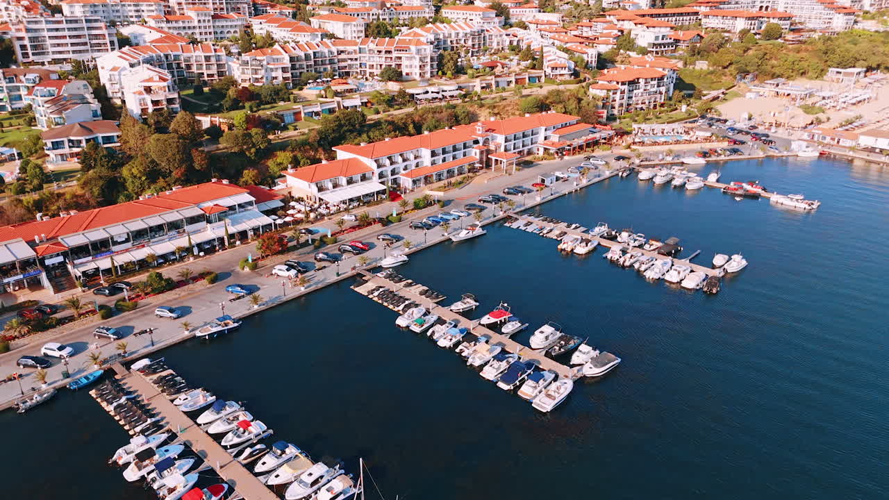 Approaching the berths with boats and jet ski scooters. Orange roofs of numerous hotels on the mountain slopes at backdrop. Sveti Vlas, Bulgaria