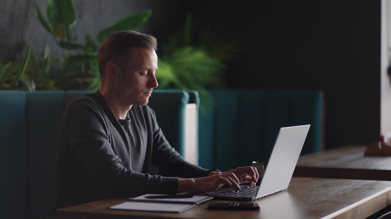 Handsome freelancer businessman in glasses diligently working on laptop in cafe. Man typing on keyboard and searches new job on internet at coffee shop. Business concept