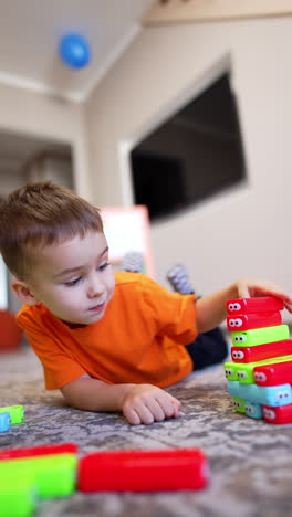 cute smiling toddler kid in orange t-shirt plays cheerfully with his toys. adorable kid builds a tower of colorful blocks. vertical video.